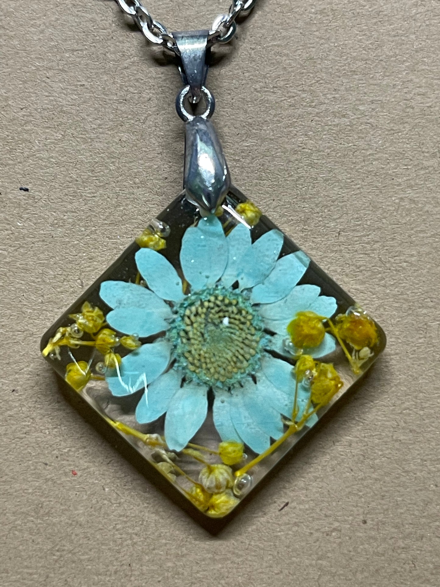 Teal daisy with baby’s breath preserved in resin on an 18” chain