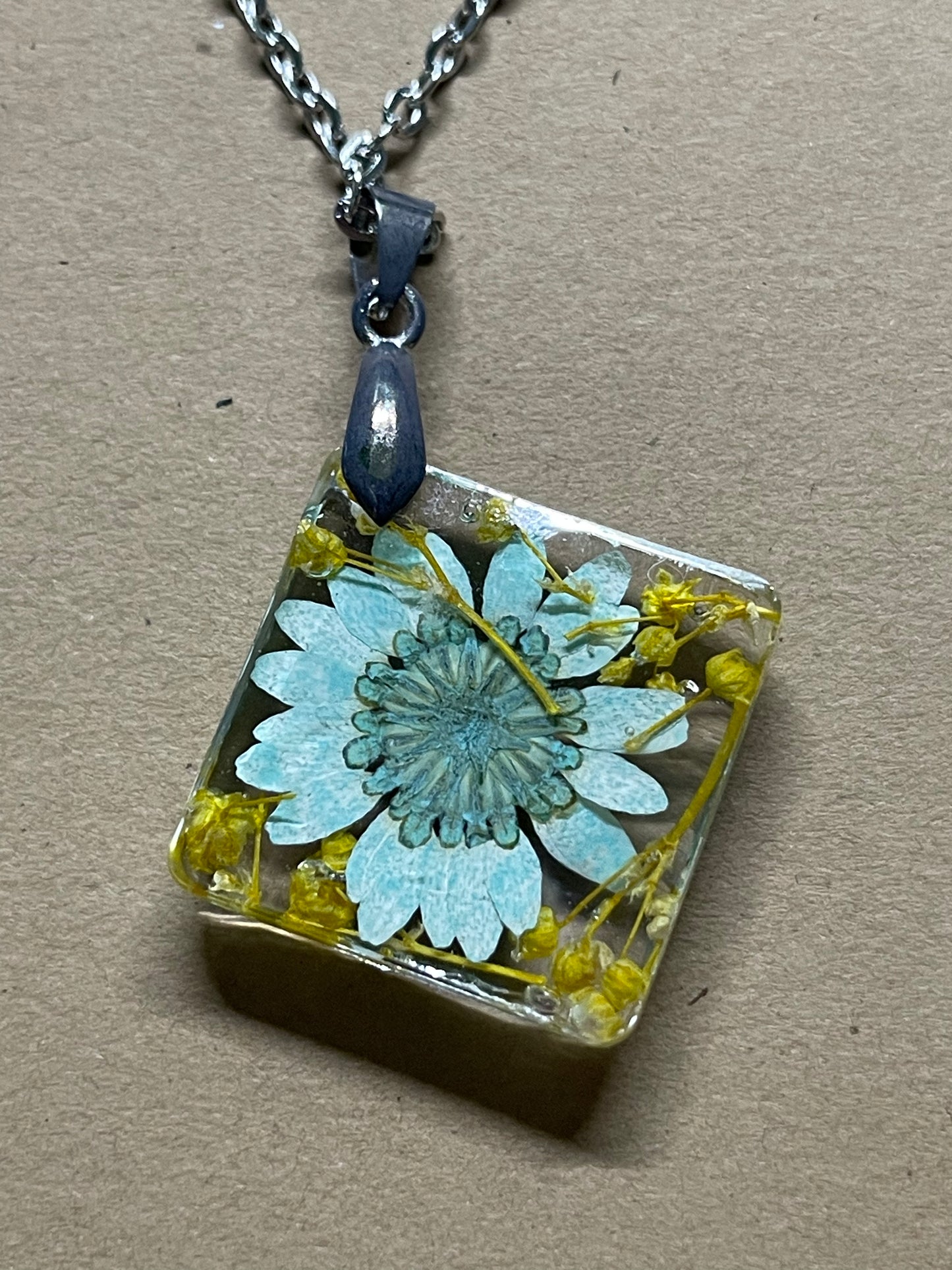 Teal daisy with baby’s breath preserved in resin on an 18” chain